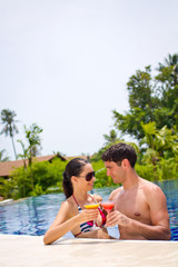 An young and attractive couple having drinks by the pool