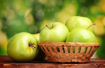 juicy green apples in basket on wooden table on green background