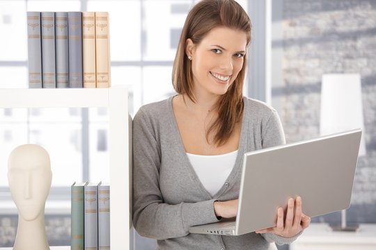 Happy woman at bookcase with computer