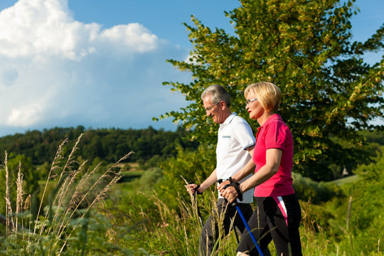 Happy mature or senior couple doing Nordic walking in summer - Powered by Adobe