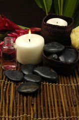 Fototapeta na wymiar burning candle and pebble with ginger flower on bamboo mat