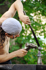 Young blacksmith hammering hot iron on anvil