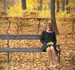 Beautiful lonely girl sitting on an autumn park bench