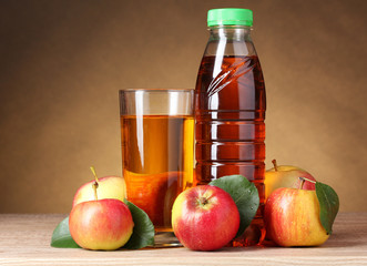 Apple juice and apples on wooden table on brown background