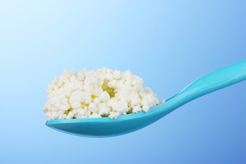 Tasty cottage cheese in spoon on blue background