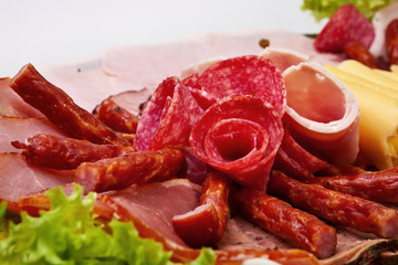 Dish with sliced ham, cheese, salami rolls and lettuce.