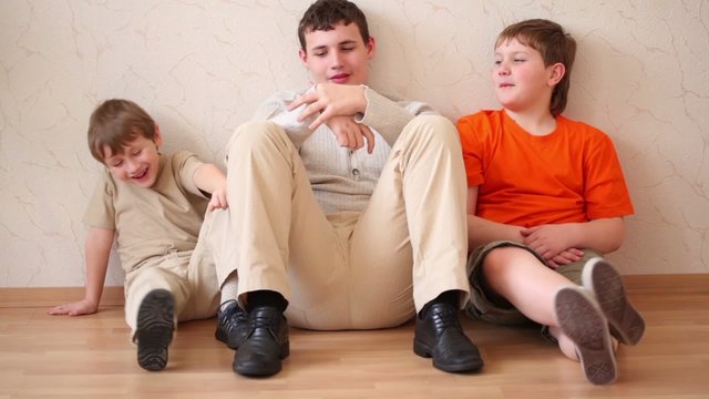 Three boys sit leaning against wall, looks forth and talk
