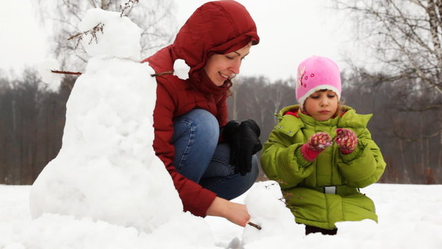 mother with little daughter make small snowman