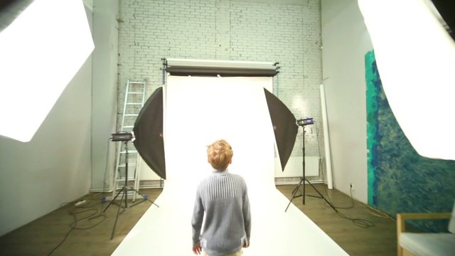 Boy walk across photo studio among spotlights
