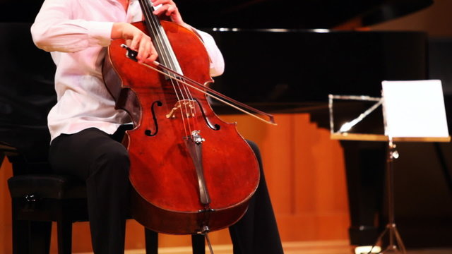 expressive young man plays cello sitting on stage
