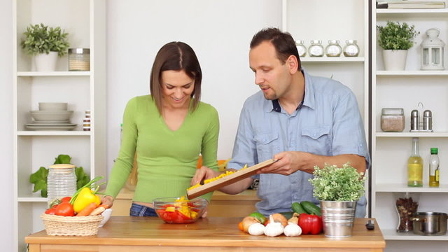 Young happy couple preparing salad at kitchen