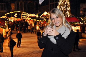 Junge Frau trinkt Glühwein auf Weihnachtsmarkt