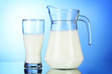 Tasty milk in jug and glass on blue background