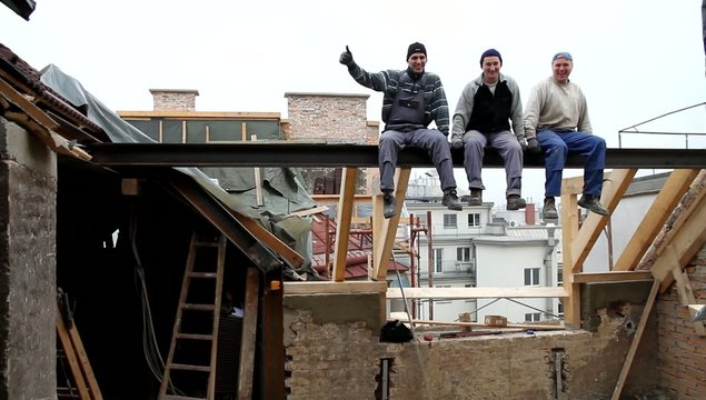 Triumphierende Arbeiter bei einem Dachausbau auf einer Traverse