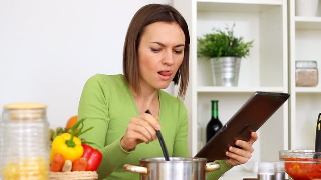 Woman cooking, tasting and looking at recipe on digital tablet