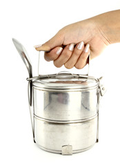 A hand holding silver metal tiffin and spoon, food container on