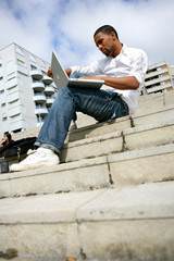 Afro-American man sitting on stairs with laptop