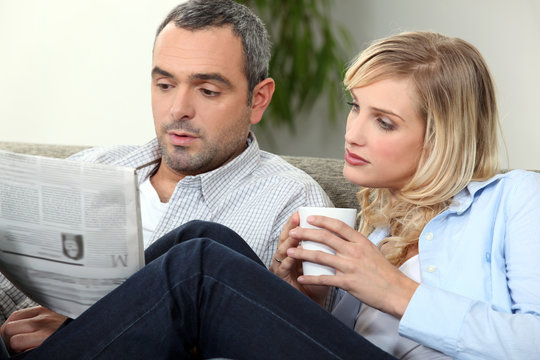 Couple Reading Newspaper On Couch