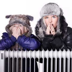 Mother and daughter in warm winter coats leaning over a radiator