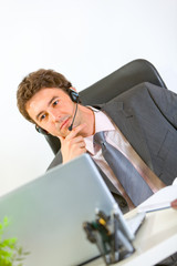 Thoughtful modern businessman with headset working on laptop
