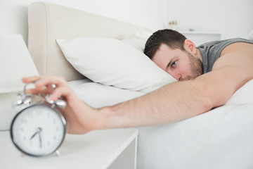 Sleeping attractive man being awakened by an alarm clock