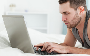 Serious man using a laptop while lying on his belly