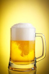 Glass of beer close-up with froth over yellow background