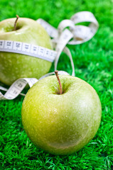 Two apples on the grass and one with a tape measure