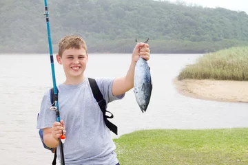 Zelfklevend Fotobehang happy teen boy showing a fishing he just caught © michaeljung