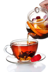 Glass teapot pouring black tea into cup isolated on white