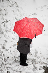 Woman with red umbrella standing in snow covered street