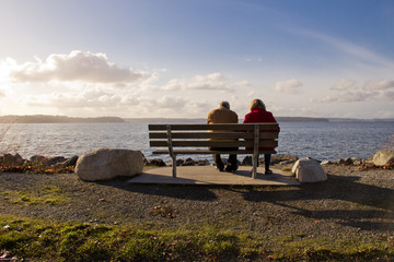 Naklejka na ściany i meble Elderly Couple Relaxing Together on Park Bench Facing a Lake
