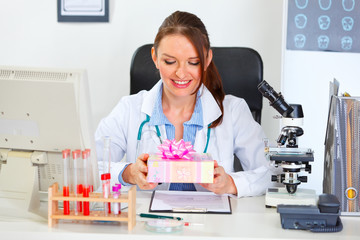 Happy doctor woman sitting in cabinet with present in hands