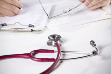 a doctor writing on note board with stethoscope on the desk.