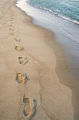 Foot imprints beside waves reaching margin. Romantic stroll.