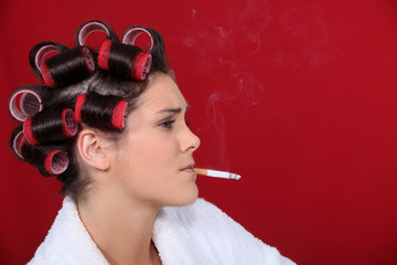 Fototapeta premium woman with hair curlers against red background smoking