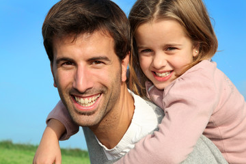 Fototapeta premium Portrait of father giving piggyback ride to daughter