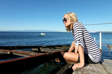 Girl is sitting on the dock near the ocean.