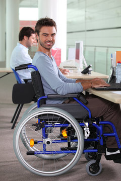 Young man in a wheelchair using a computer in the workplace