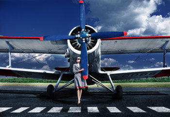 The girl in a checkered raincoat poses at the plane