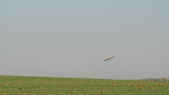 Yellow spray plane fly over a green field
