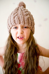 Angry child girl in beige knitted hat