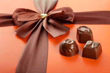 Milk chocolates and beautiful gift box with ribbon bow, closeup