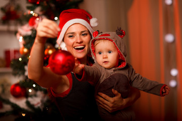 Mother showing Christmas ball  to baby near Christmas tree