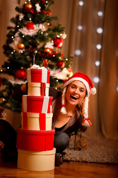 Woman near Christmas tree looking out from pile of presens