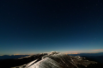 Naklejka premium Glittering stars above snowy autumn mountain ridge