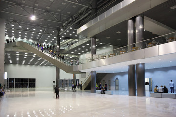 People stand and walk in lobby, at escalator and second floor