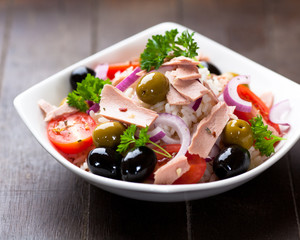 Tuna and rice salad with olives on wooden board