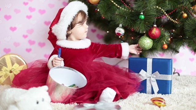 Baby girl with xmas gifts sitting near a Christmas tree