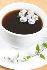 Cup of tea with flowers of peppermint floating in it
